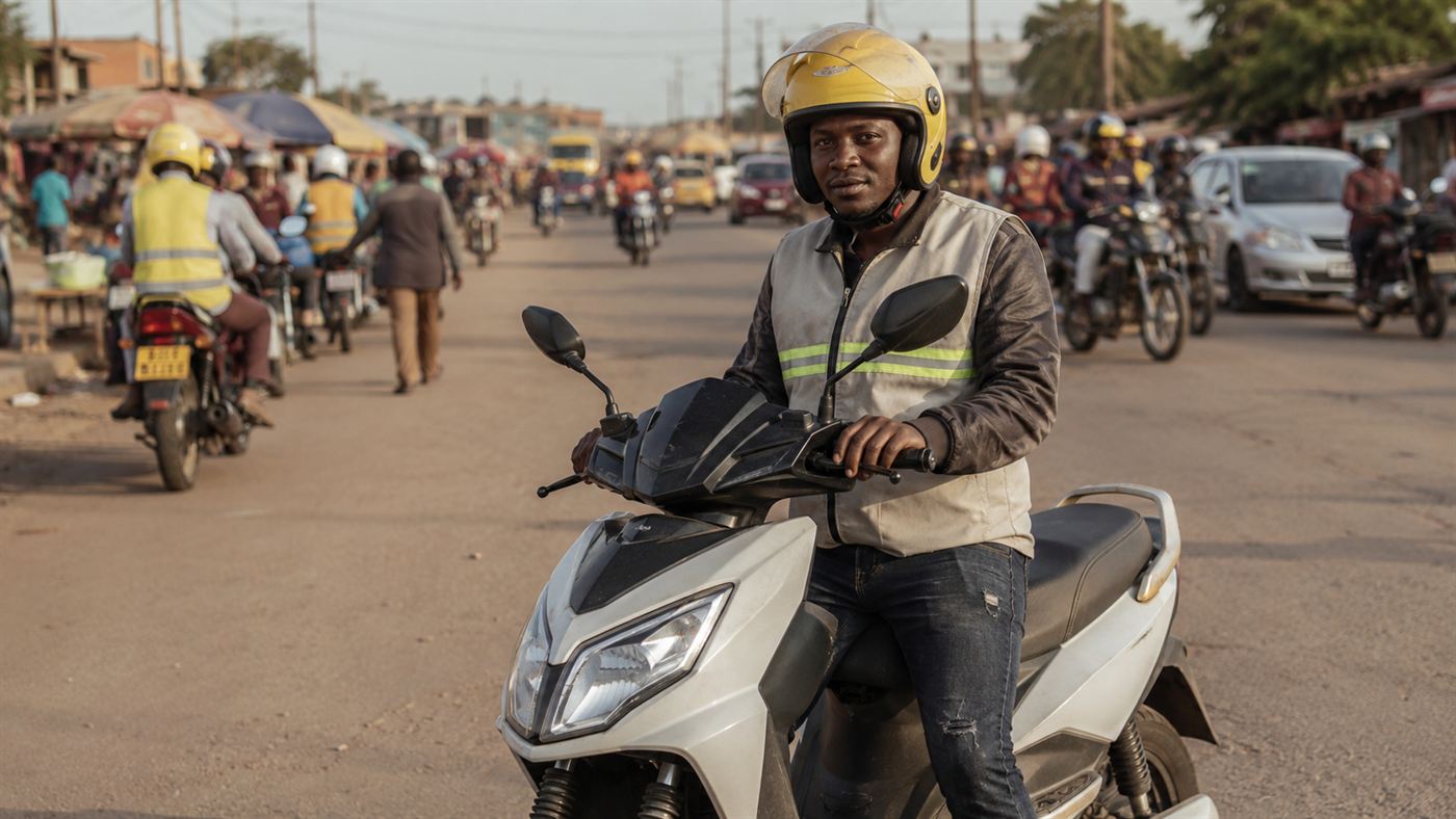 A motorcycle-taxi rider on an electric motorbike on a busy African city street with other riders and traffic behind