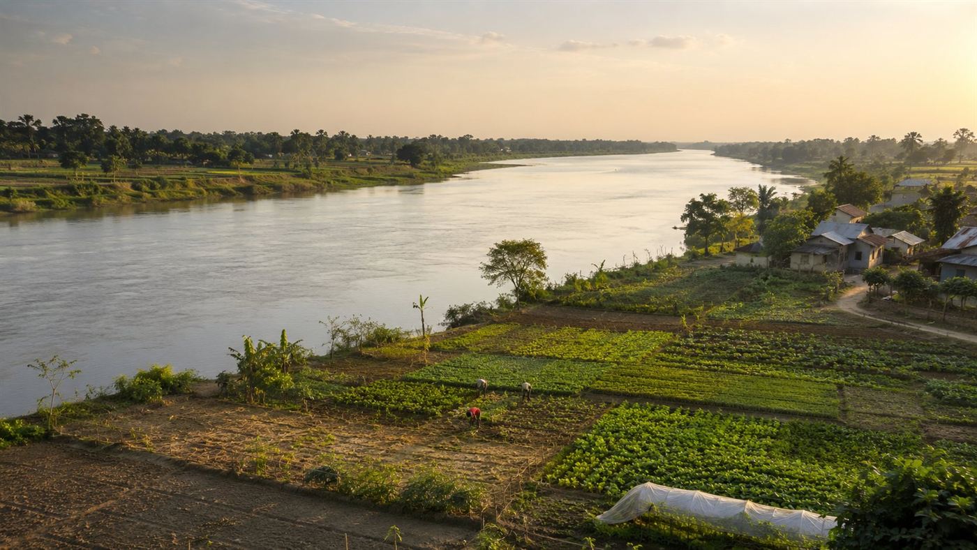 The wide Brahmaputra river flowing past green farmland and villages downstream in India and Bangladesh