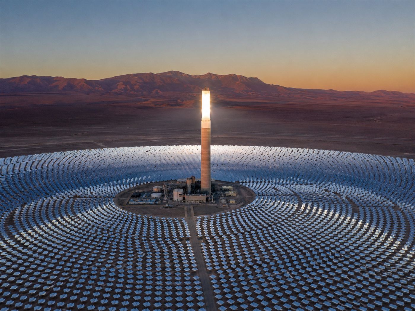 A glowing concentrated solar power tower ringed by thousands of mirrors in the Atacama desert at dusk