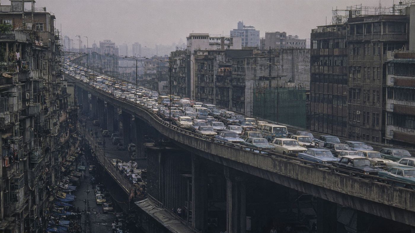 An old grey elevated concrete motorway packed with traffic running through a dense Asian city, covering the ground completely, before the restoration