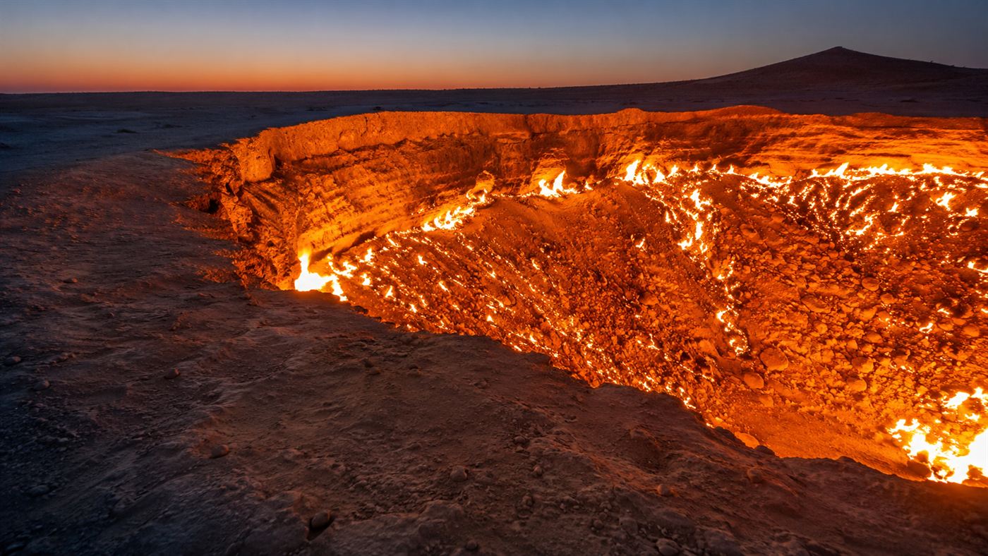 Close view of the rim of the Darvaza gas crater at dusk with flames and glowing embers rising from the pit in the desert