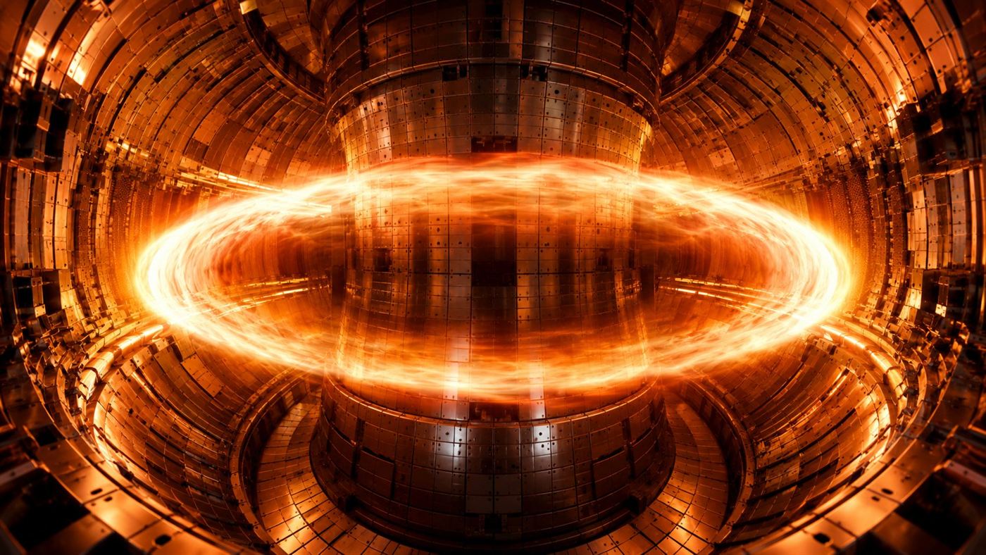 The glowing interior of a doughnut-shaped tokamak fusion reactor with a ring of superheated orange plasma swirling inside