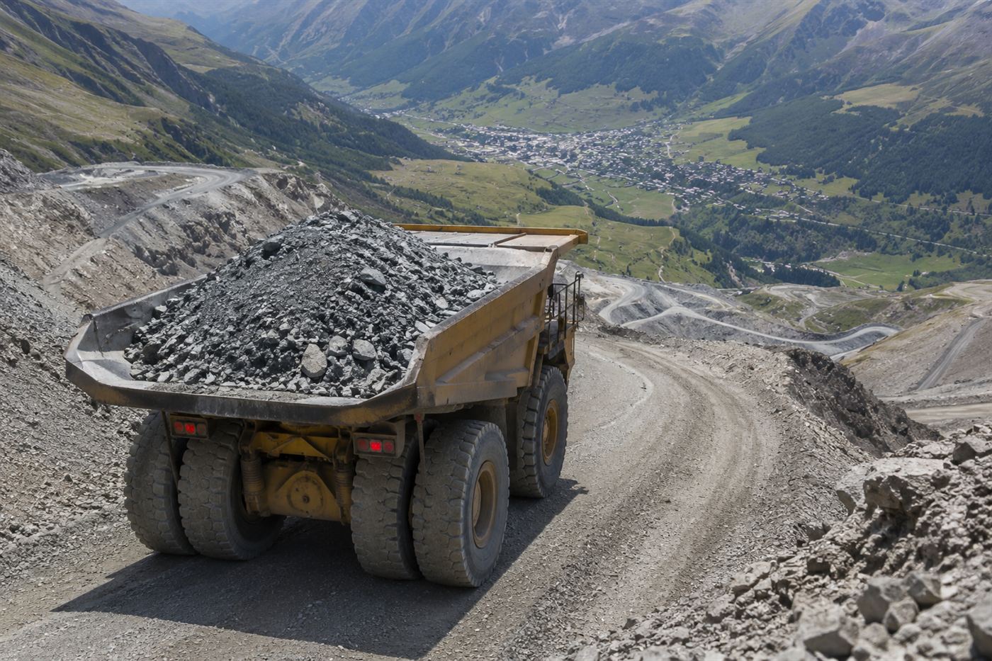 A loaded electric mining truck descending a steep quarry road with an alpine valley spread out below