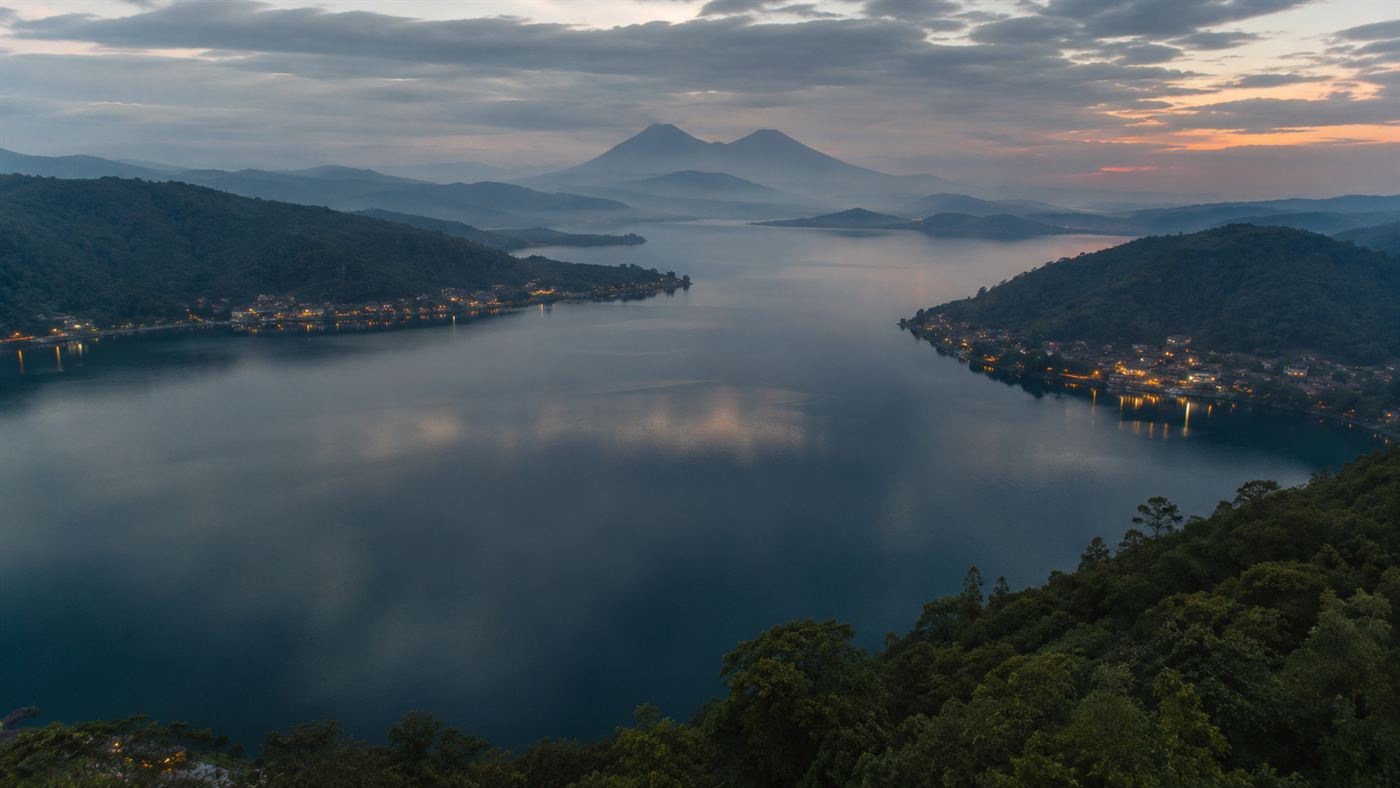 A vast calm African lake at dusk ringed by green volcanic hills and lakeside towns