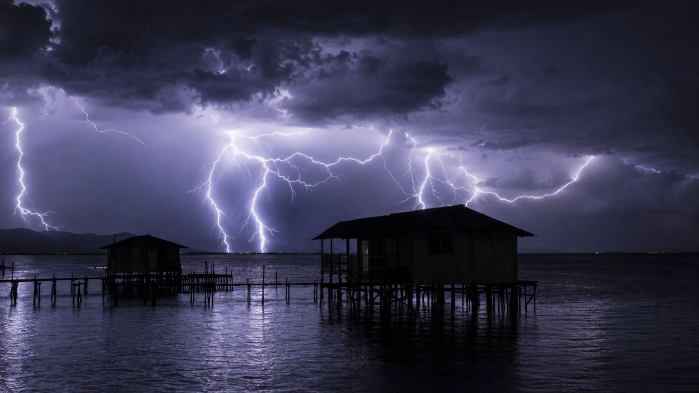 Lightning flashing over Lake Maracaibo at night behind silhouettes of wooden stilt houses on the water with mountains in the distance