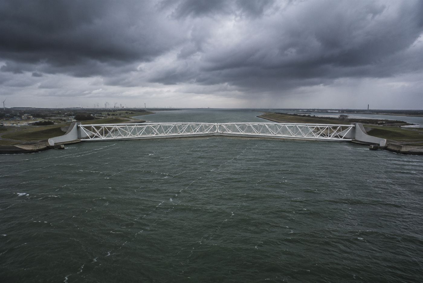 The two huge white arms of the Maeslant barrier swung out and meeting in the middle of the canal under a stormy grey sky