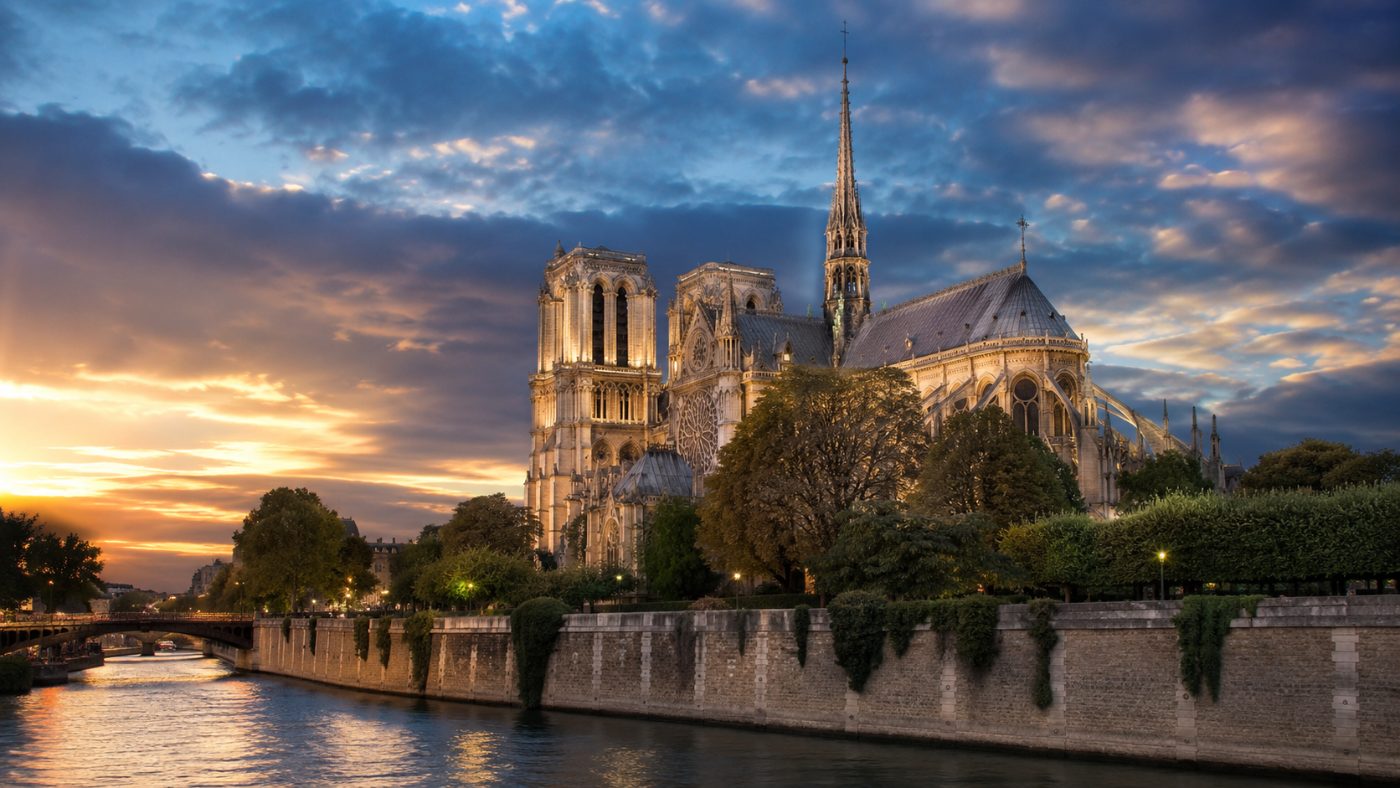 The restored Notre-Dame de Paris cathedral with its rebuilt spire glowing under a dramatic evening sky across the Seine