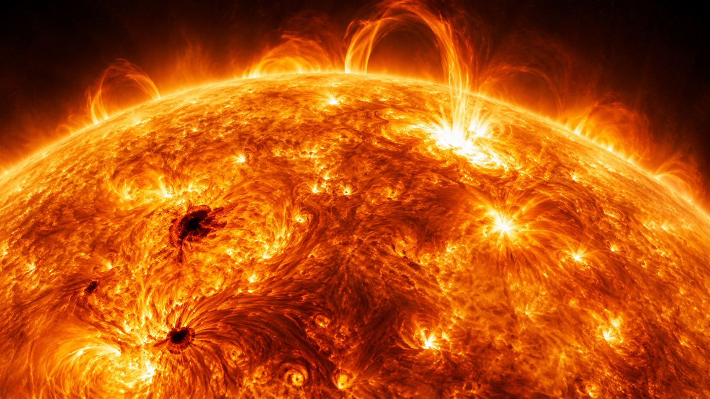 A close view of the turbulent glowing orange surface and outer atmosphere of the Sun with arcs of plasma and bright flares