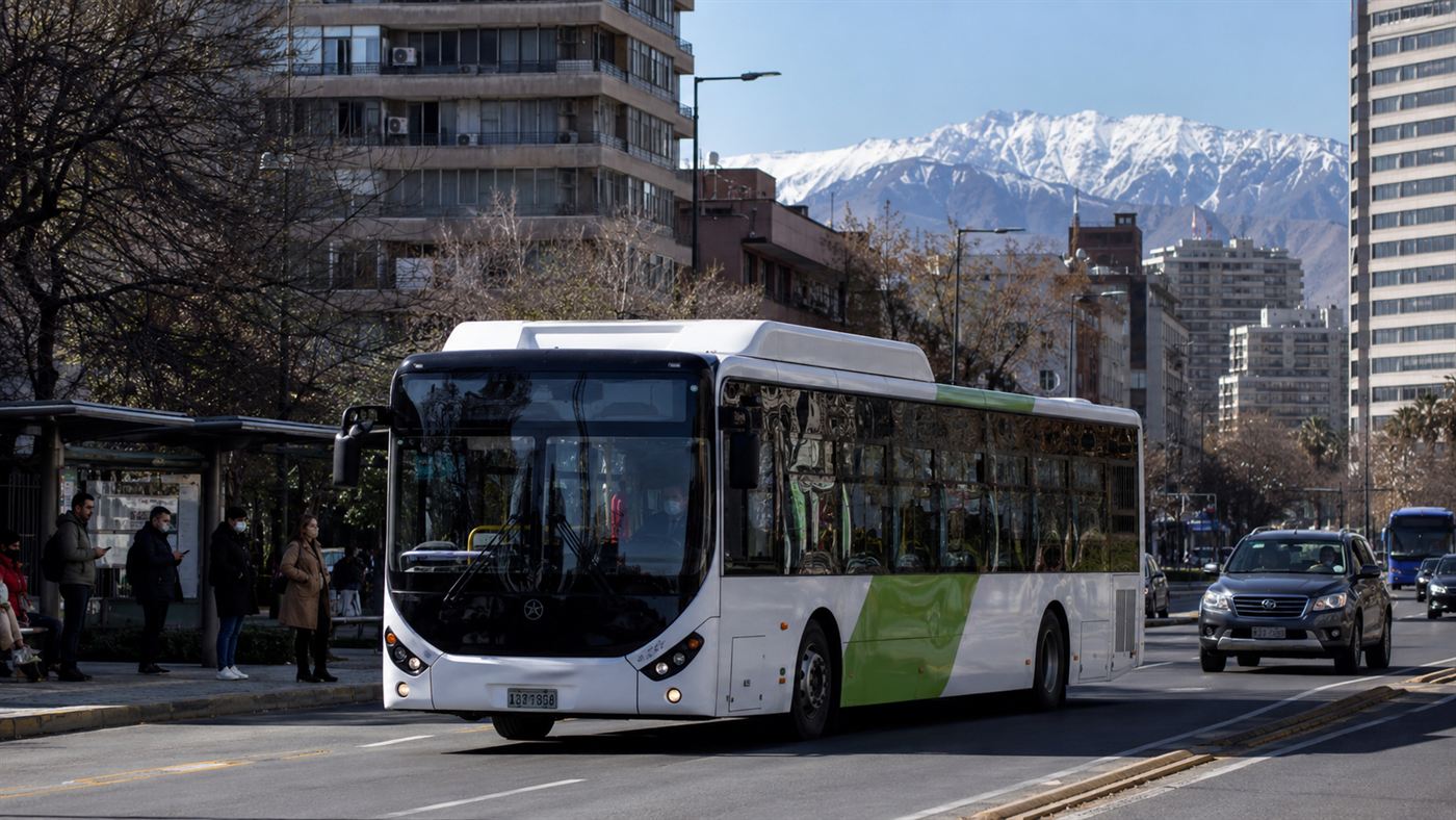 A modern electric city bus on a Santiago street with the snow-capped Andes rising behind the buildings