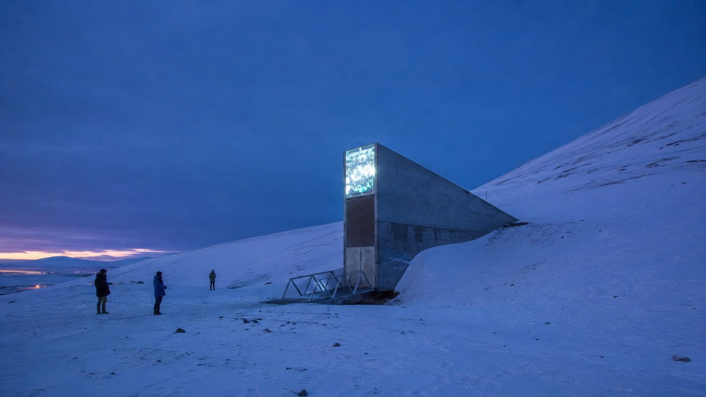 The wedge-shaped concrete entrance of the Svalbard Global Seed Vault jutting from a snow-covered Arctic mountainside at polar twilight