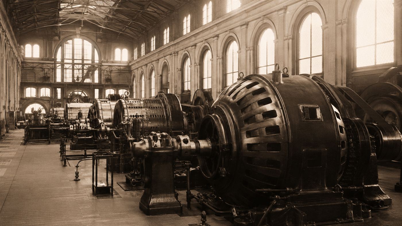 A grand powerhouse hall around 1895 filled with enormous early alternating current dynamo generators and iron machinery
