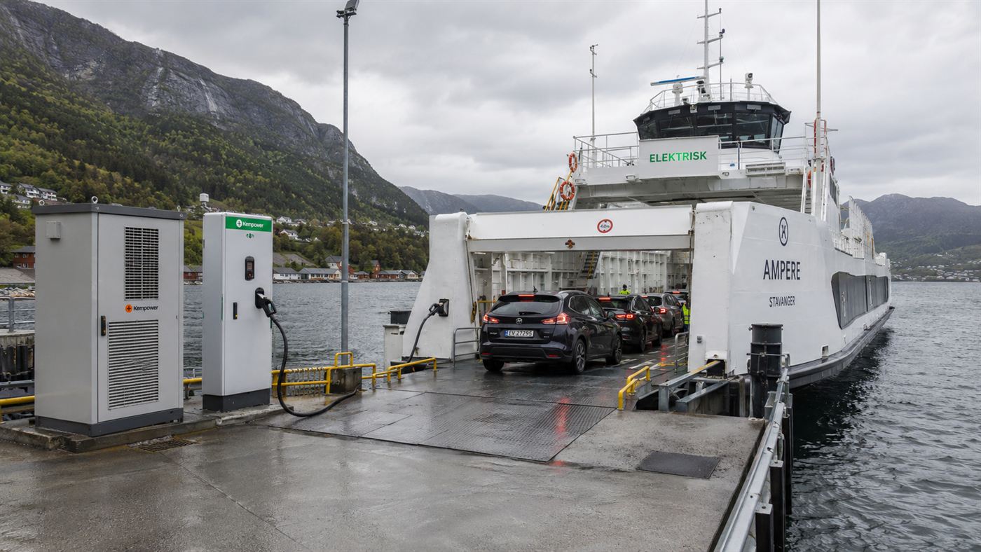 The Ampere ferry docked at a fjord pier connected to a shoreside charging station and battery cabinet