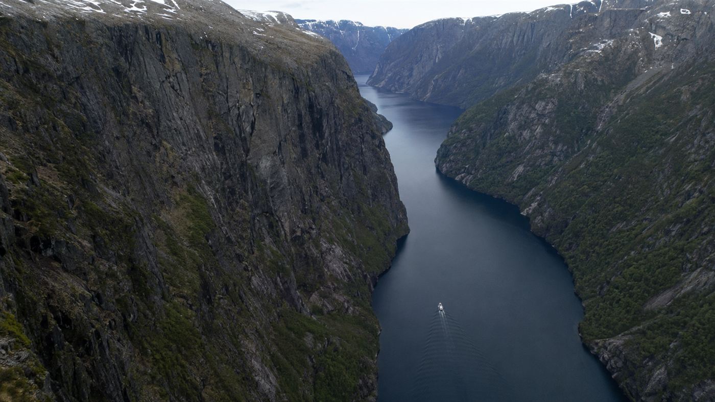 A wide view of the Ampere ferry small against the vast steep walls of a deep Norwegian fjord