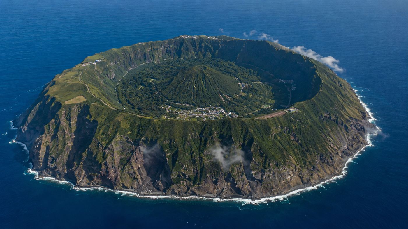 An aerial view of Aogashima, a remote volcano island in the Pacific that is one giant green crater with a smaller cone and a village inside