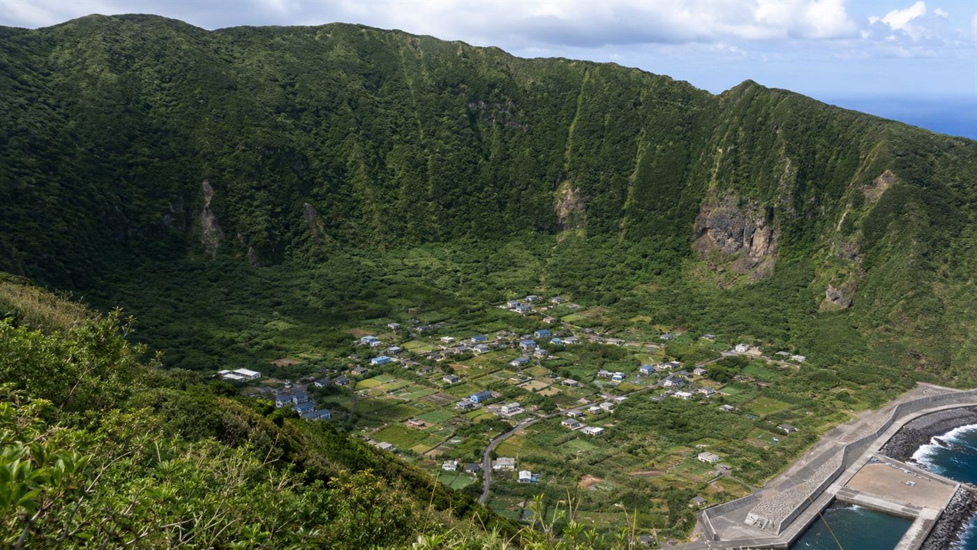 The village of Aogashima nestled inside the outer crater of the active volcano, small houses and green fields below the caldera rim