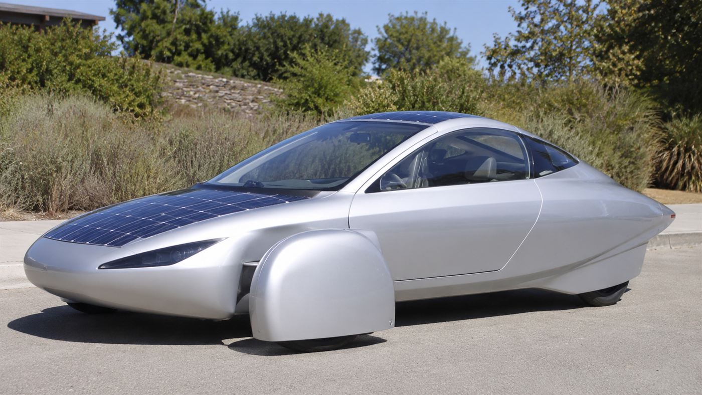 The Aptera, a sleek teardrop-shaped three-wheeled solar electric car parked in sunshine