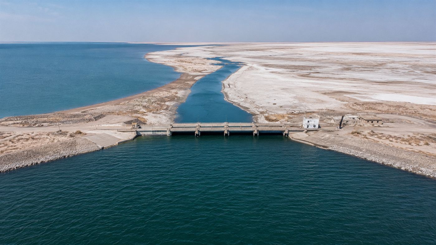 The Kokaral Dam across a narrow strait of the North Aral Sea in Kazakhstan, with blue water visible on one side and dry salt flats on the other, aerial view