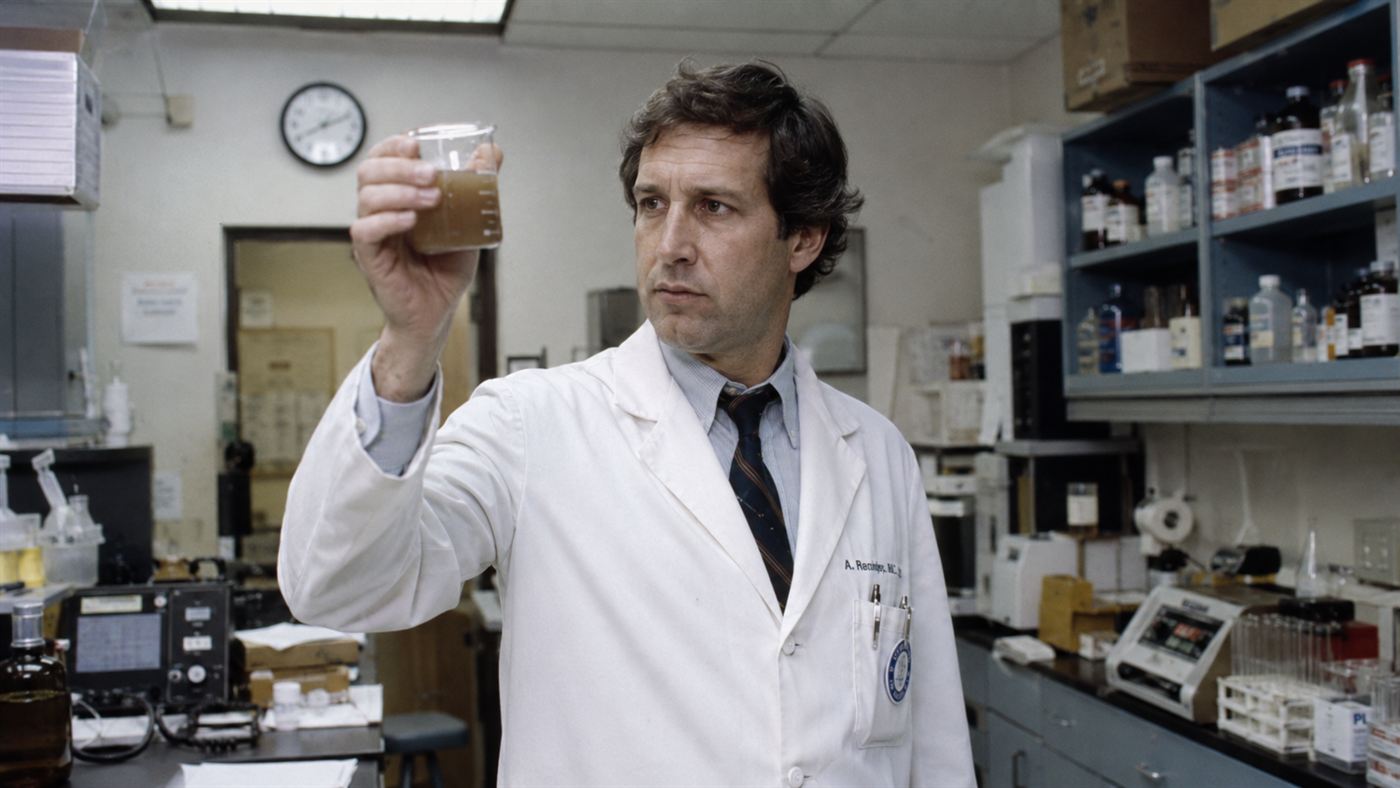 Barry Marshall, a 1980s doctor, holding a beaker of murky liquid culture in a laboratory