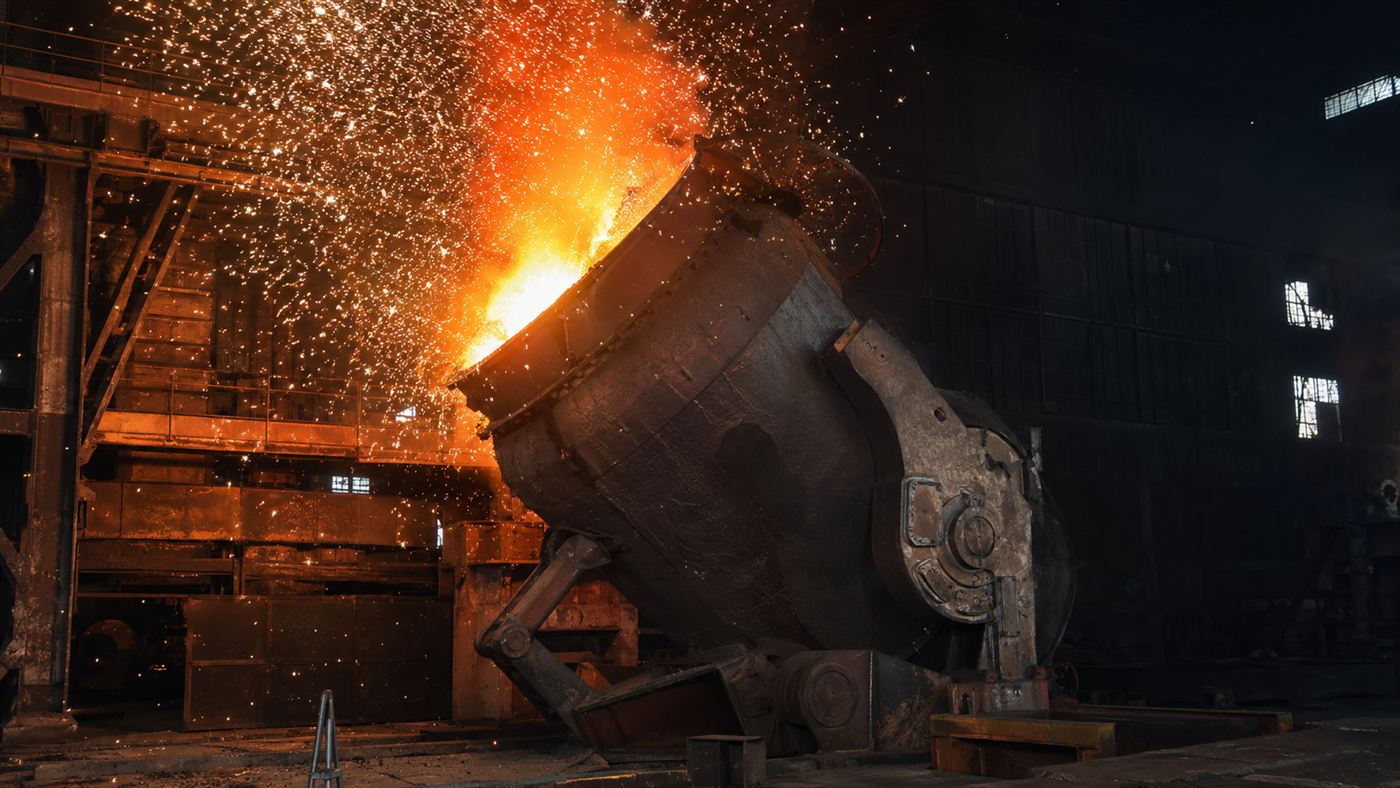 A 19th-century Bessemer converter erupting in a fountain of orange and white sparks inside a dark steel mill
