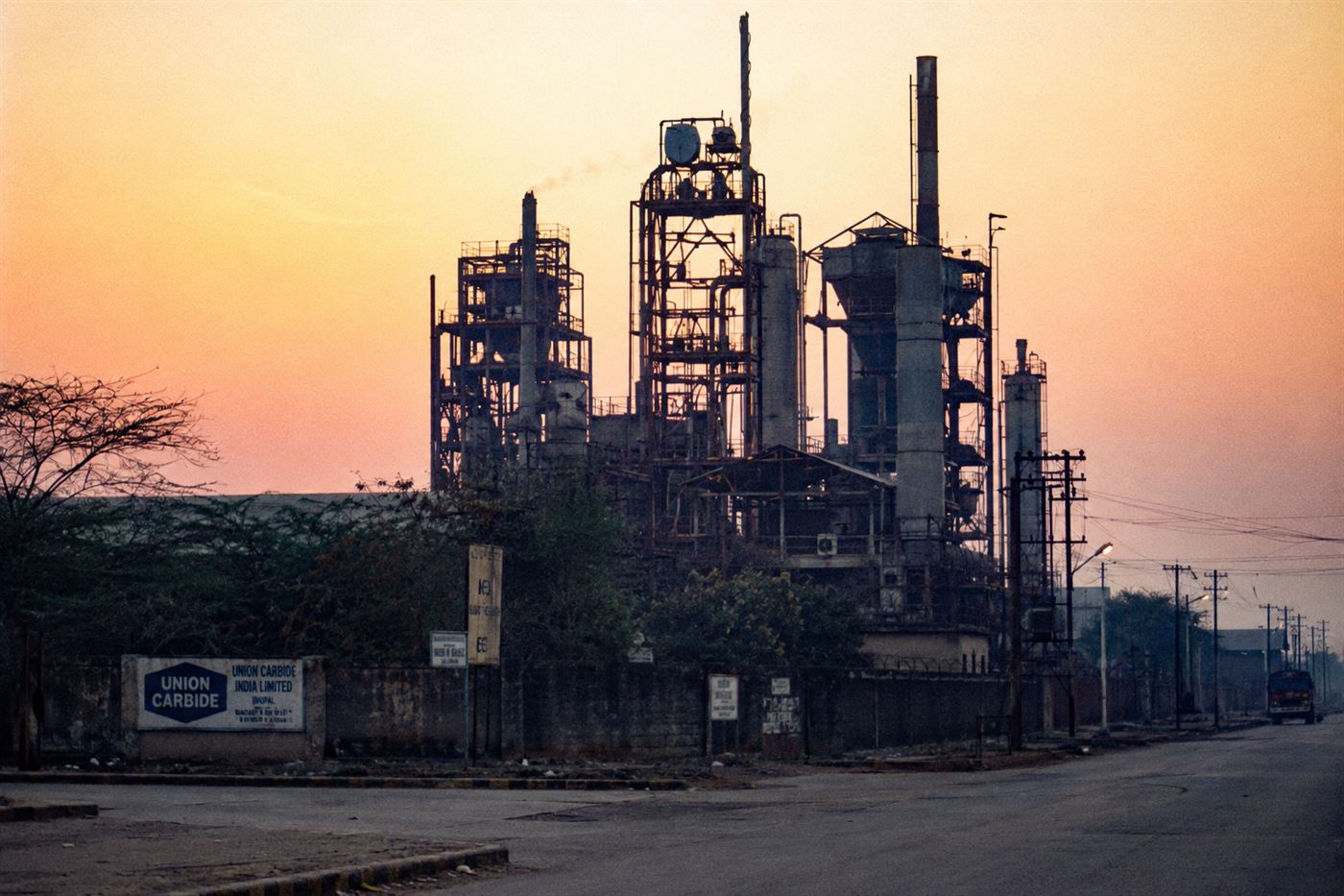The Union Carbide pesticide factory in Bhopal India at dawn, industrial plant with smokestacks, empty streets below, moody dramatic light