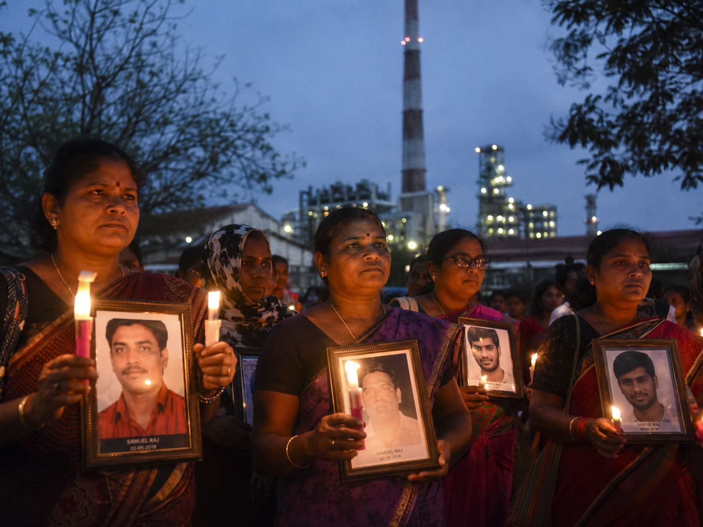 Survivors of the 1984 Bhopal gas disaster, Indian women activists holding candles and photographs of the dead at a memorial vigil near the abandoned Union Carbide factory, dignified and powerful social documentary scene at dusk