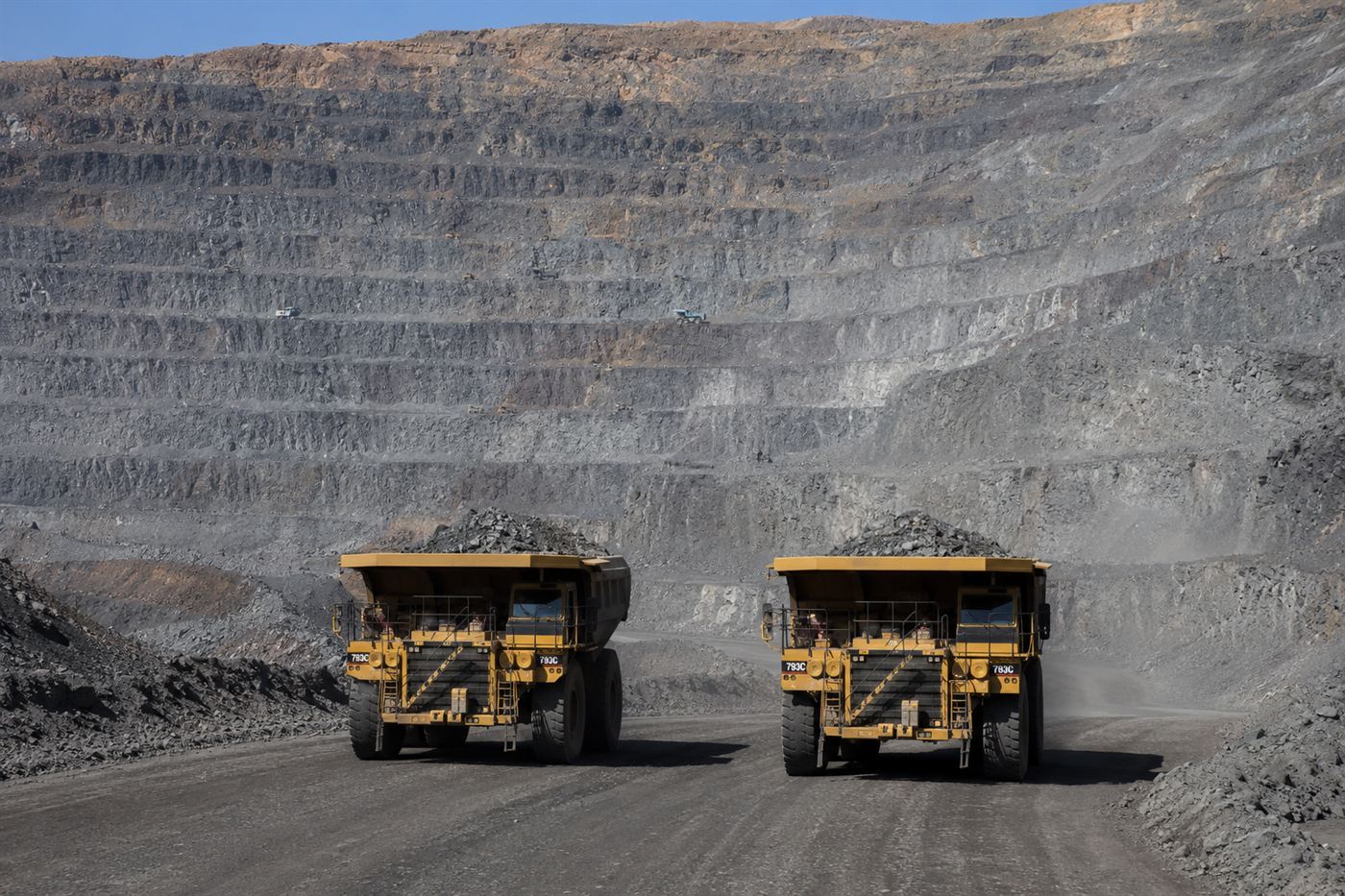 Enormous mining haul trucks on the wide terraced roads of the Bingham Canyon pit, dwarfed by the scale of the excavation