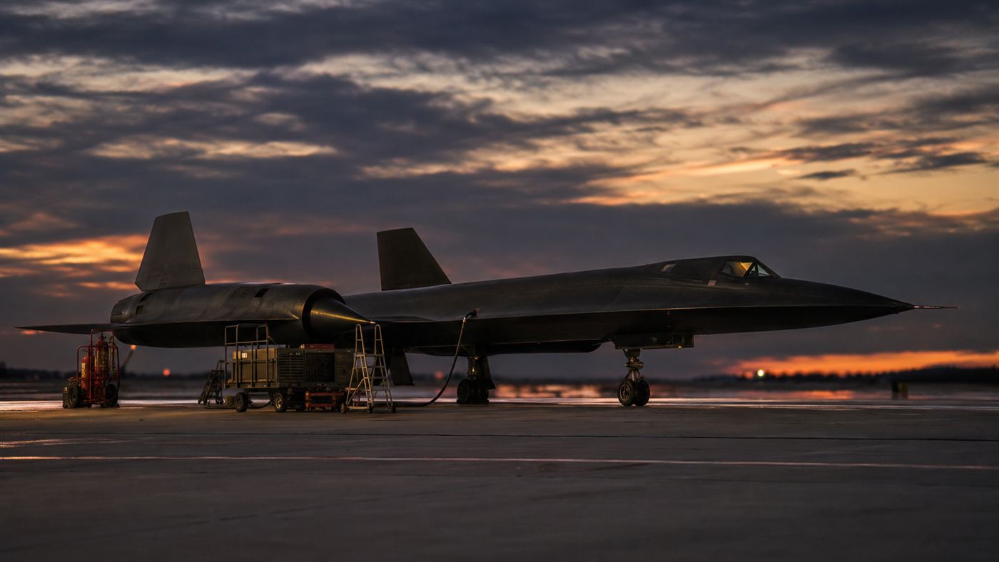 A black Mach 3 reconnaissance jet parked on a runway at dusk with heat haze