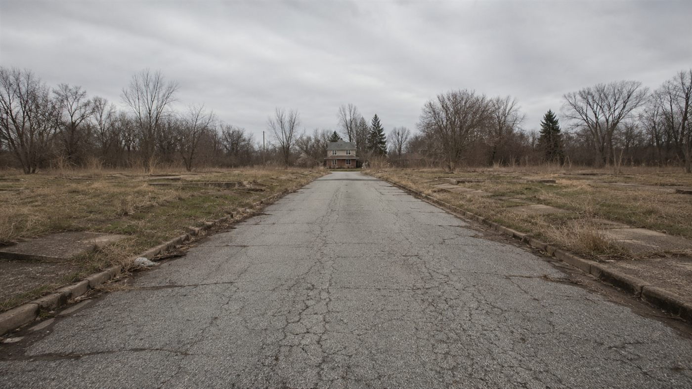 An empty residential street in a ghost town with cracked pavement and overgrown vacant lots