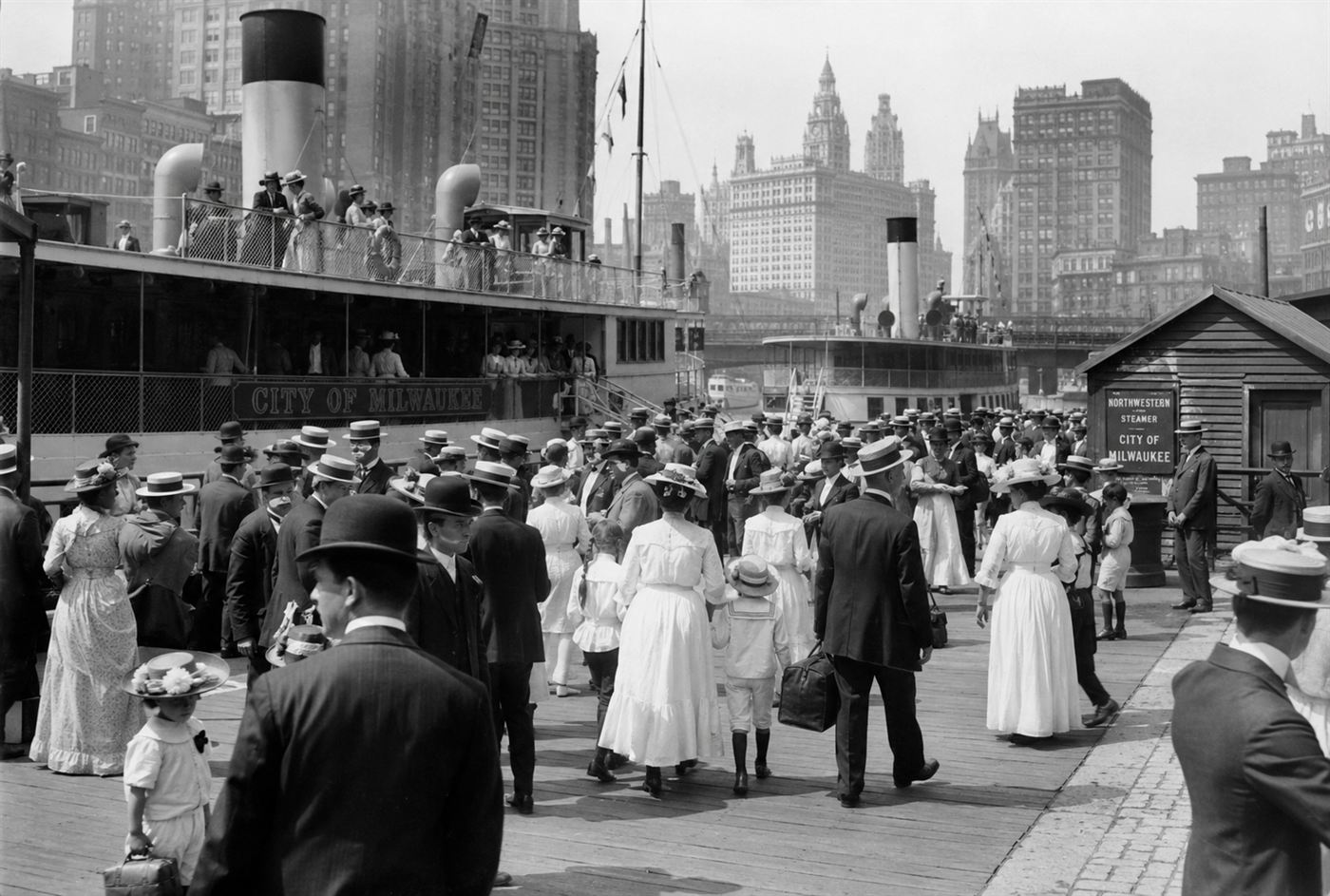 Crowds of well-dressed workers and families at a dock on the Chicago River in 1915, passenger steamships moored at the waterfront, urban waterfront scene