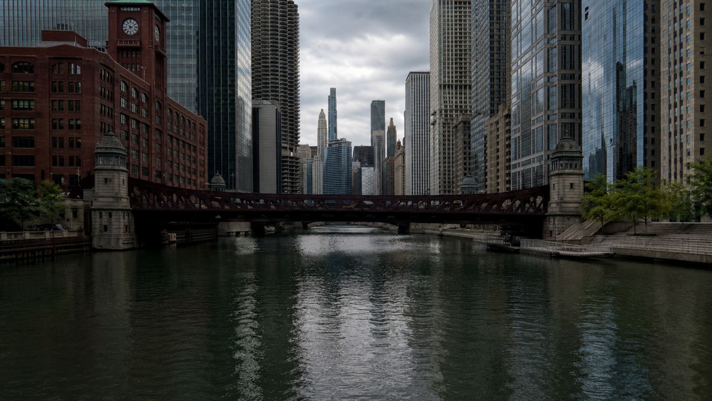 The Chicago River flowing through downtown Chicago between skyscrapers and bridges under an overcast sky
