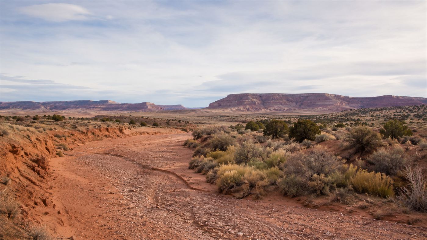 A dry reddish riverbed of the Puerco River winding through arid New Mexico high desert scrub and mesas near Church Rock under a wide sky