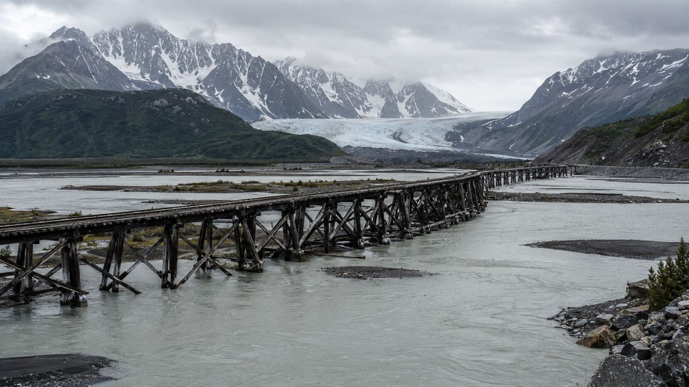 A wooden railroad trestle of the Copper River and Northwestern Railway crossing a glacial river in Alaska