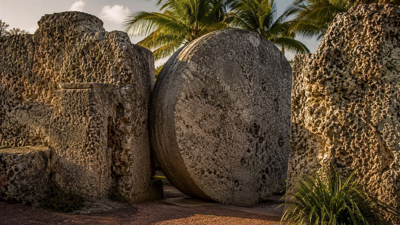 The massive nine-ton revolving stone gate of Coral Castle standing between rough limestone walls in the Florida light
