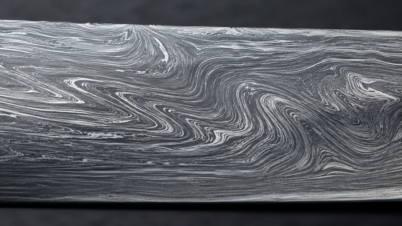 Extreme close-up of the rippling banded light and dark watered pattern across the surface of a Damascus steel blade