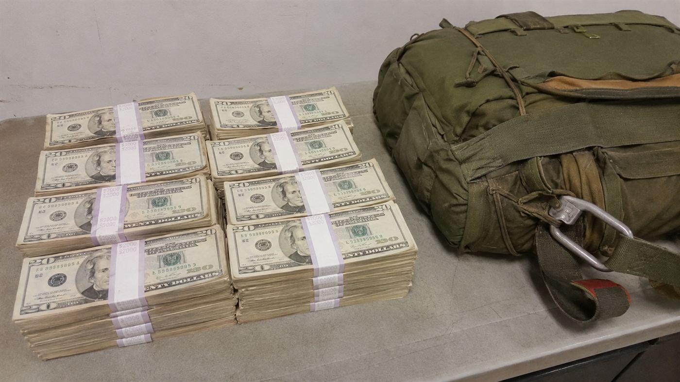 Stacks of 1970s twenty-dollar bills beside a folded parachute pack on a table