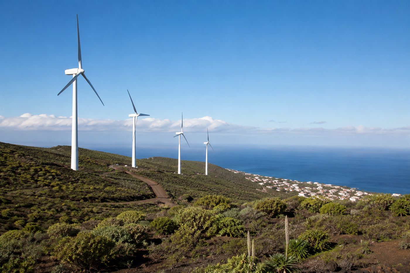 Five white wind turbines on the volcanic hills of El Hierro above the coast