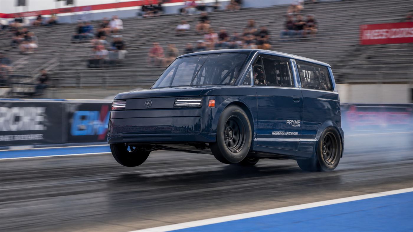 A small heavily modified electric drag car launching hard down a strip with its front wheels lifting