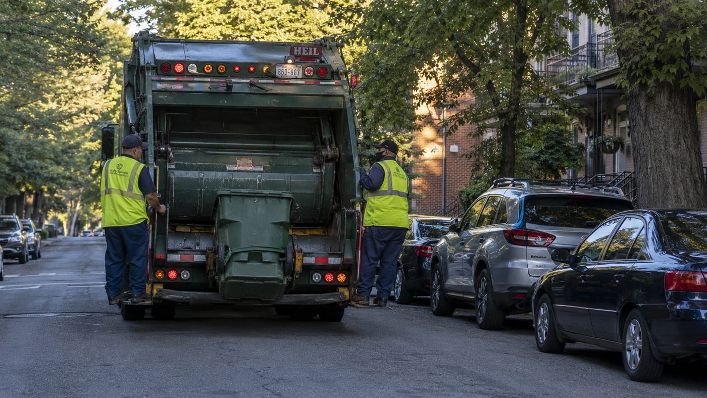 A garbage truck collecting bins on a quiet city street, the kind Wrightspeed converts to an electric powertrain