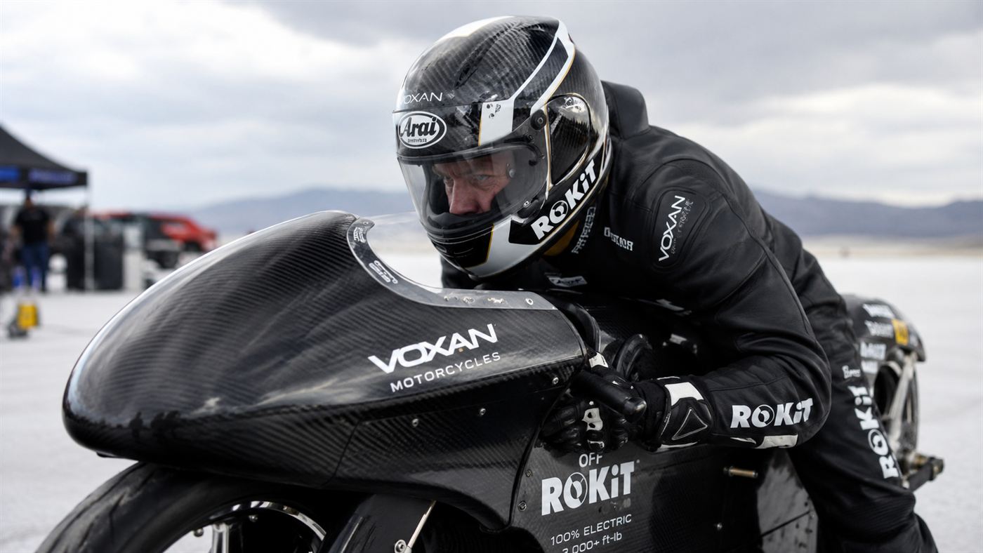 A racer in aerodynamic leathers and full-face helmet crouched on a sleek black electric record motorcycle