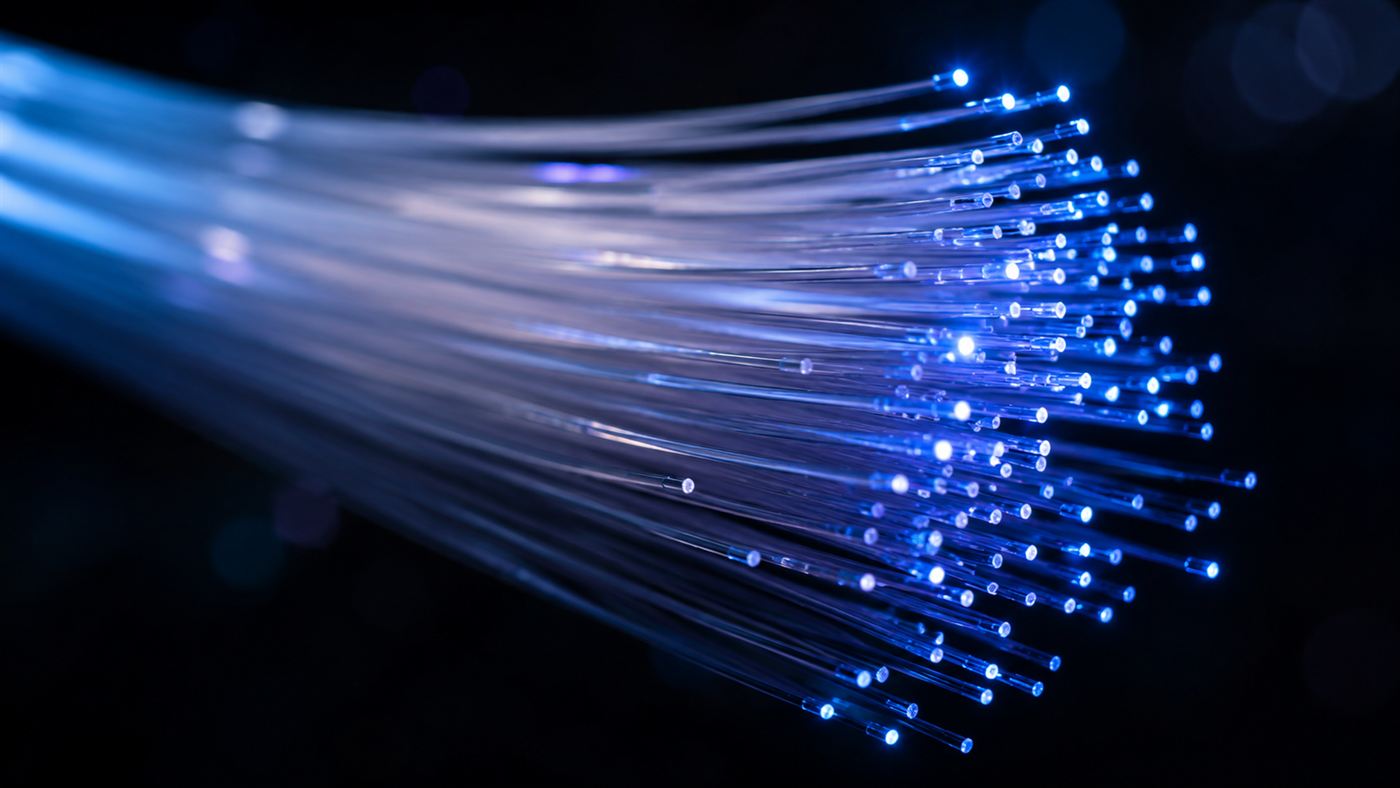 A bundle of glowing glass fiber-optic strands carrying points of coloured light in the dark