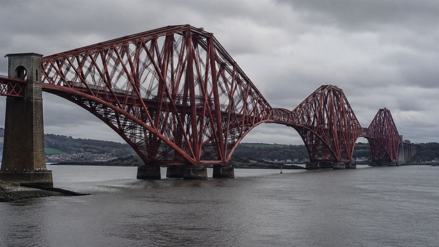 The deep-red steel cantilever Forth Bridge spanning the Firth of Forth in Scotland with a train crossing