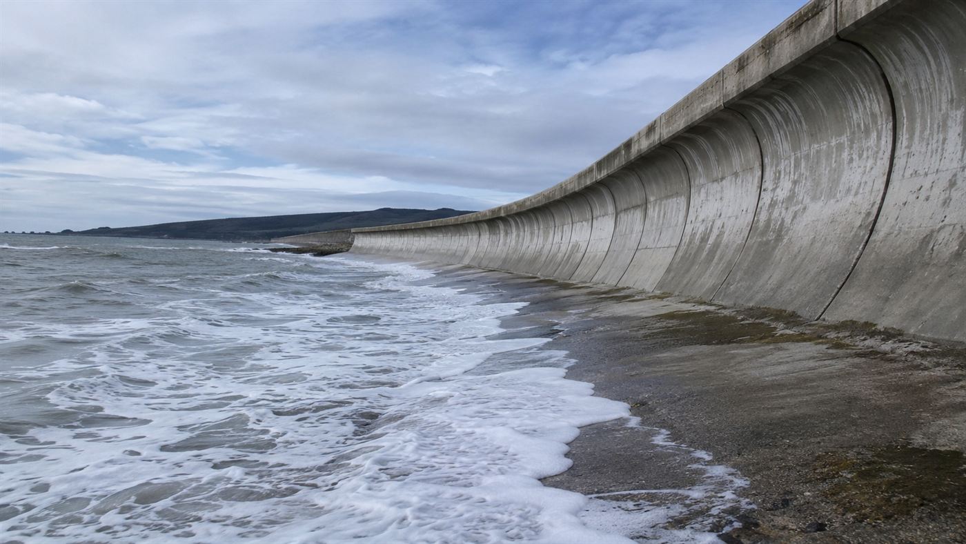 A long curved concrete seawall holding back grey ocean waves, the Galveston seawall