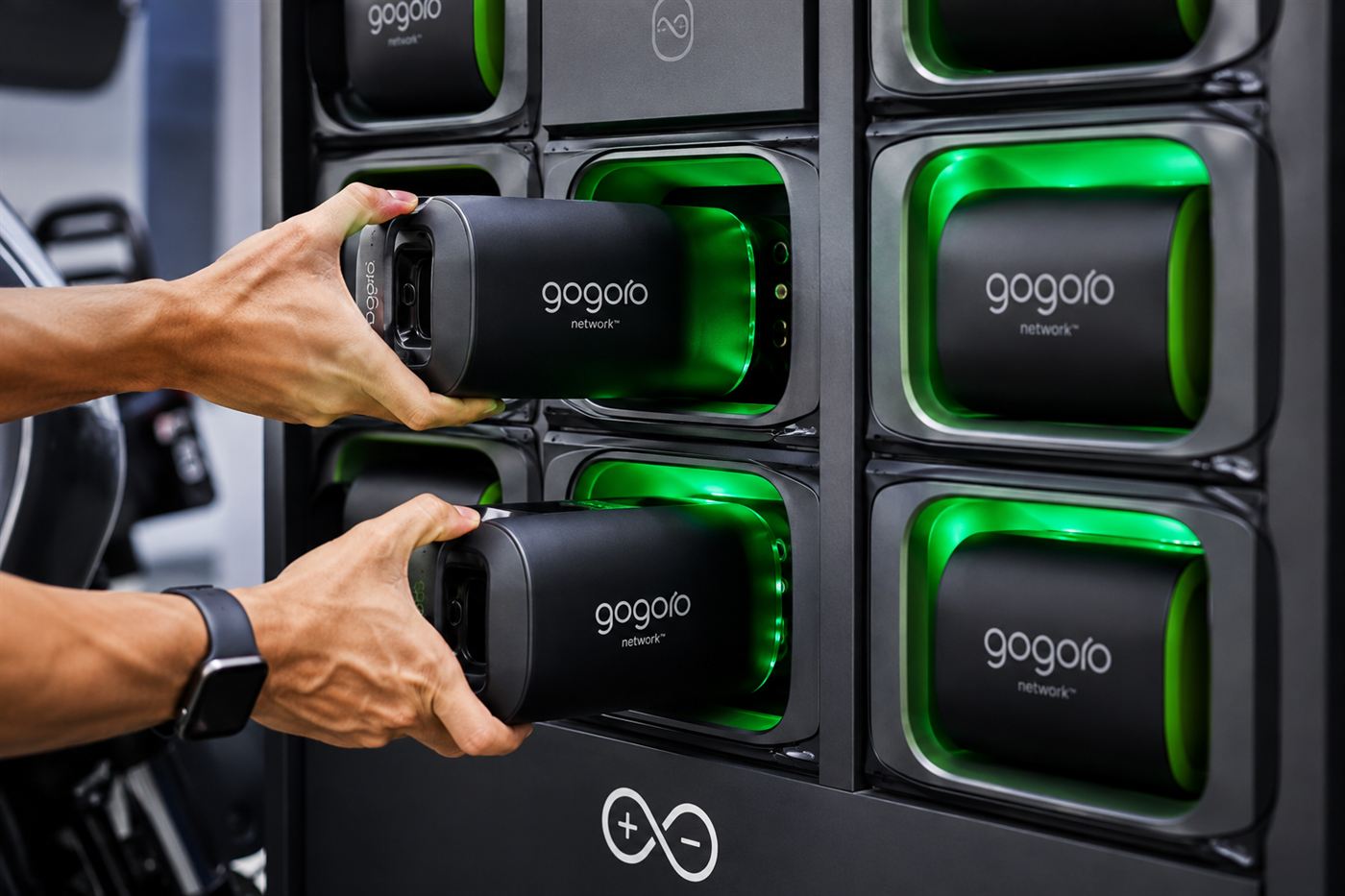 Close-up of two Gogoro batteries being slotted into the glowing green charging bays of a GoStation cabinet