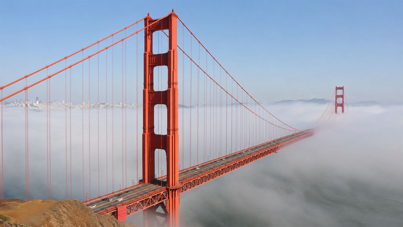 The finished Golden Gate Bridge in International Orange with its towers rising out of rolling fog