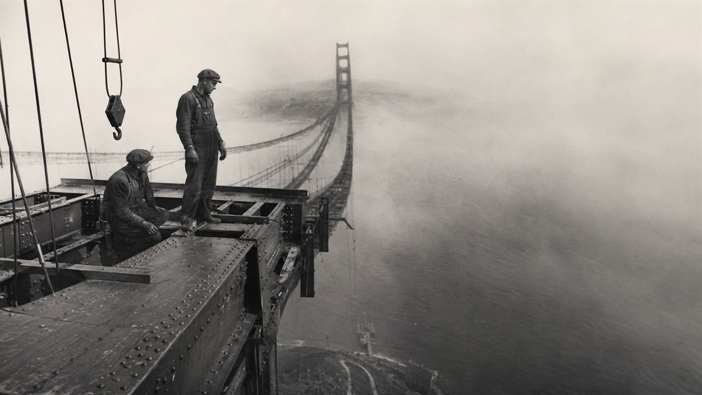 Ironworkers balancing on the high steel of a Golden Gate Bridge tower wreathed in fog during construction
