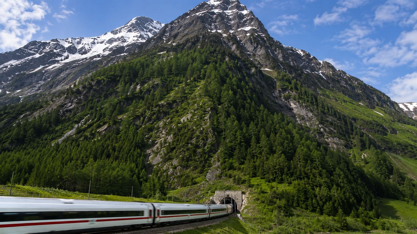 A high-speed train entering the Gotthard Base Tunnel portal at the foot of the towering Swiss Alps