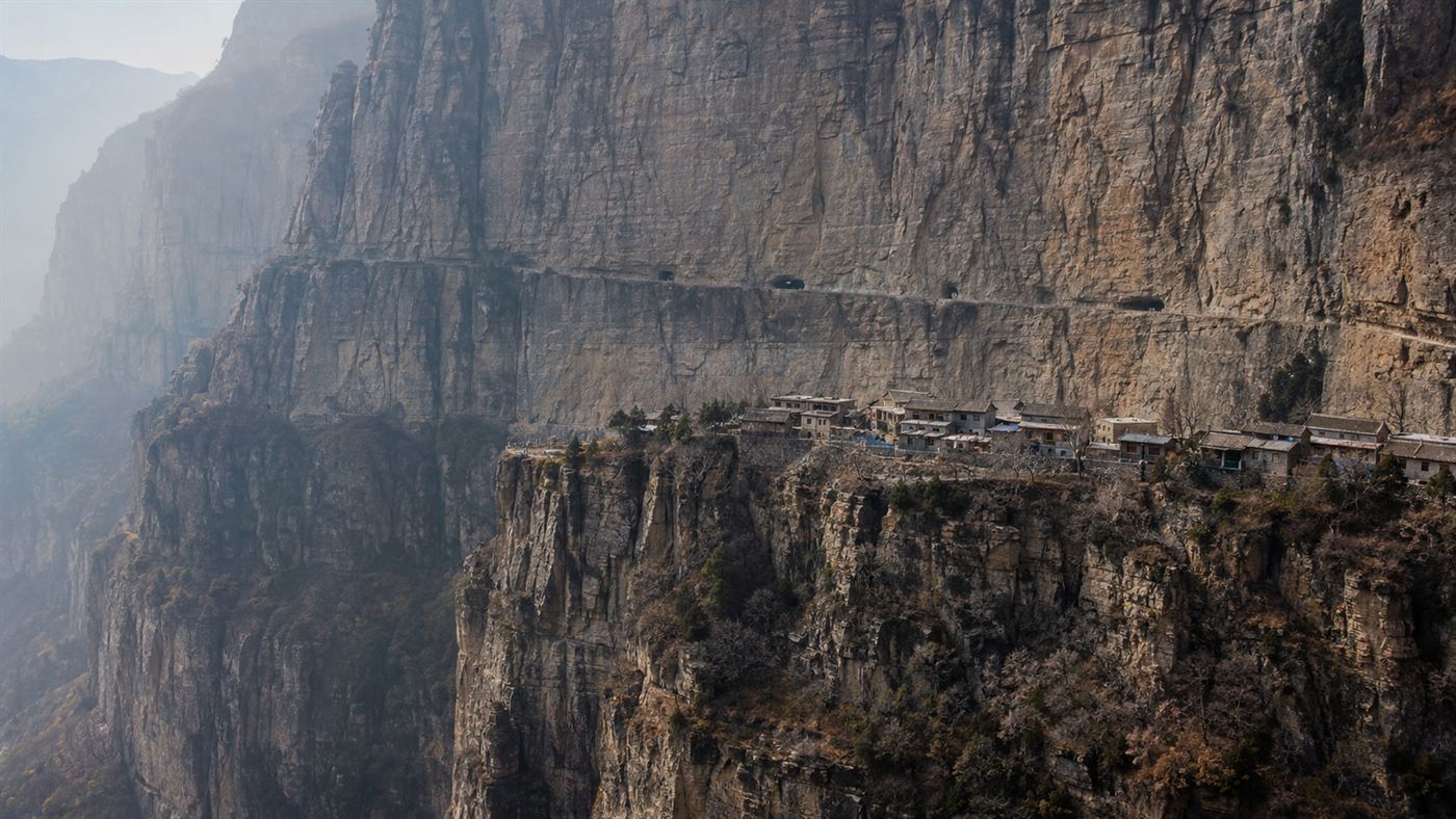 A vast vertical cliff in the Taihang Mountains with a remote stone village perched above a deep gorge near the Guoliang Tunnel