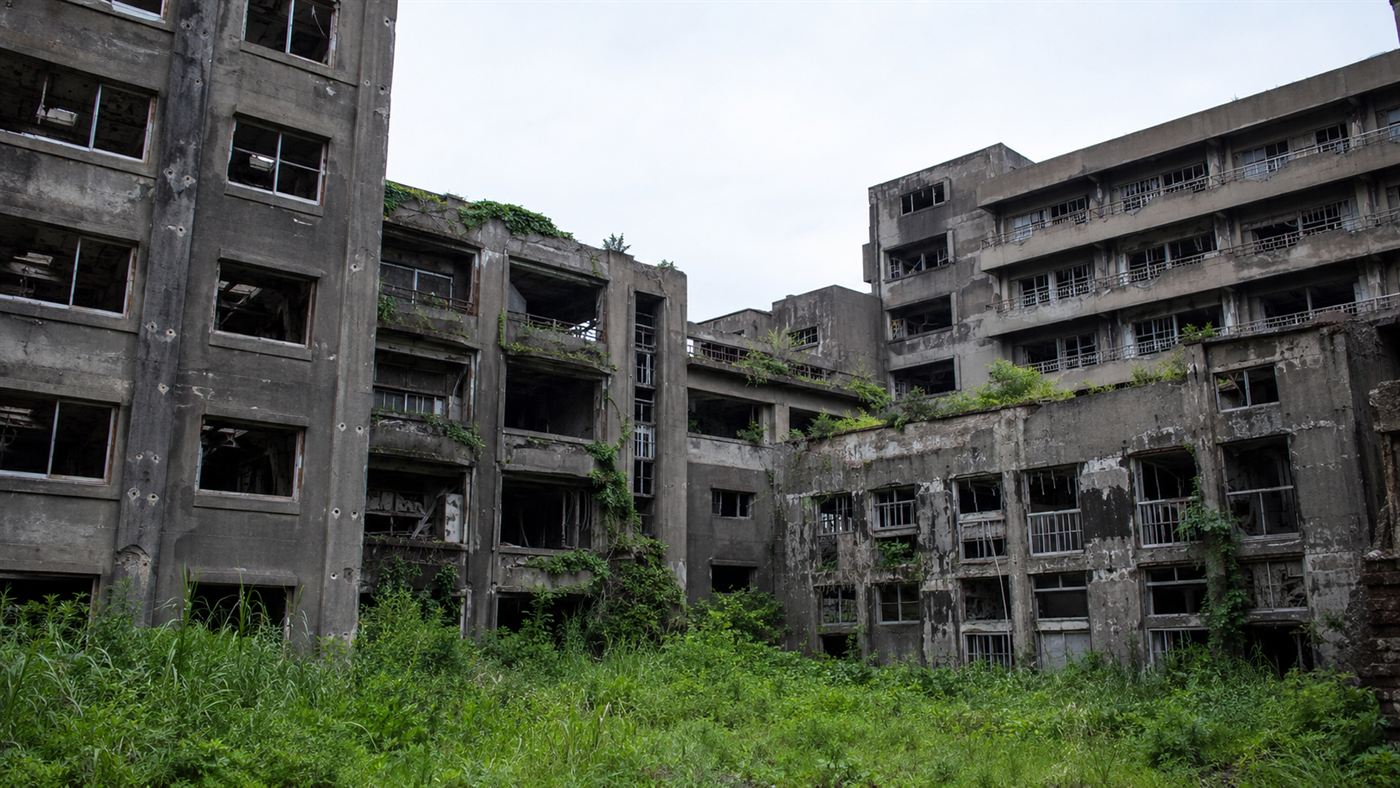 Crumbling abandoned apartment blocks overgrown with weeds on Hashima Island, where thousands of coal miners once lived