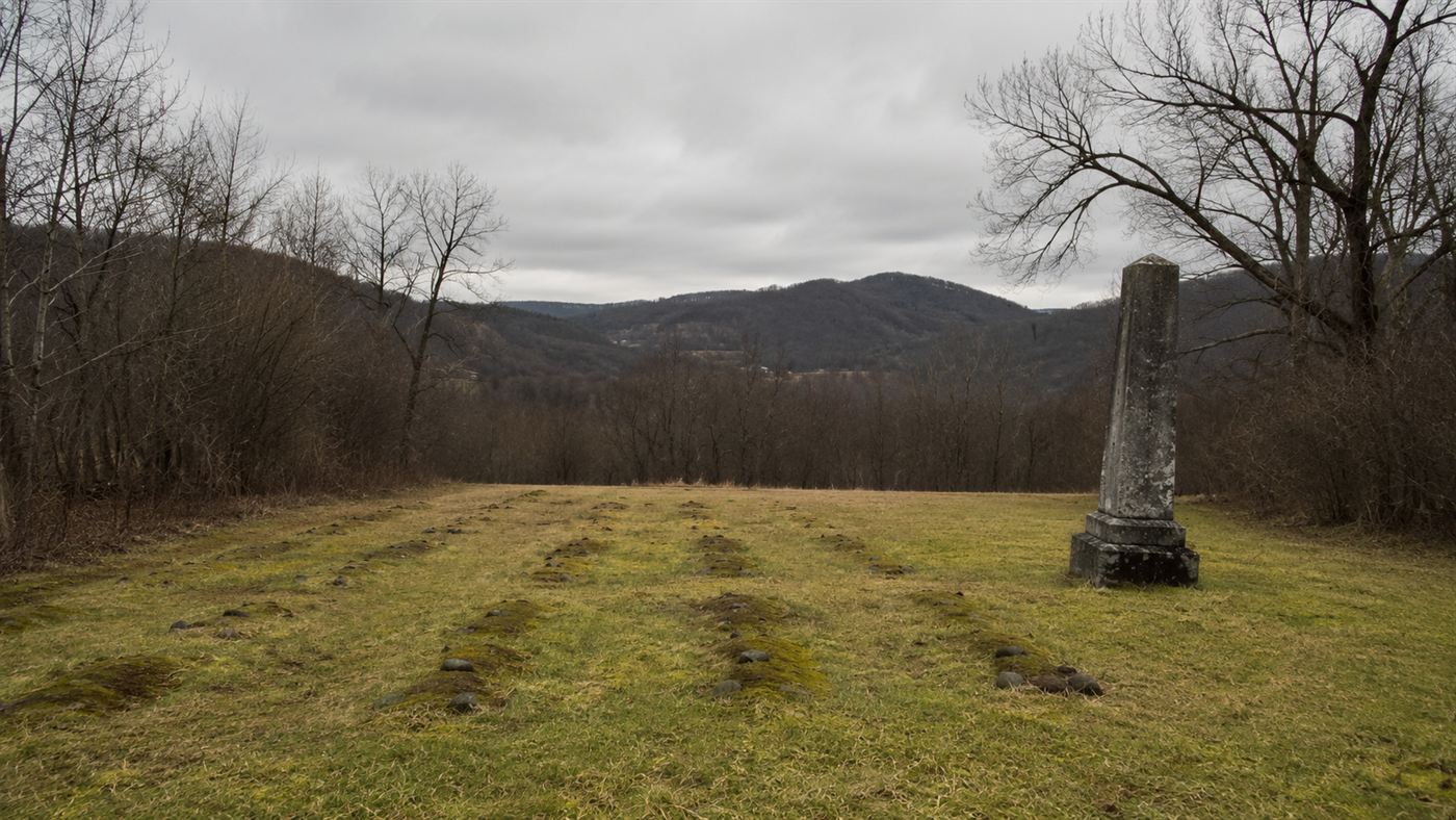 Rows of unmarked graves and a weathered stone memorial in a West Virginia field commemorating Hawks Nest Tunnel disaster victims