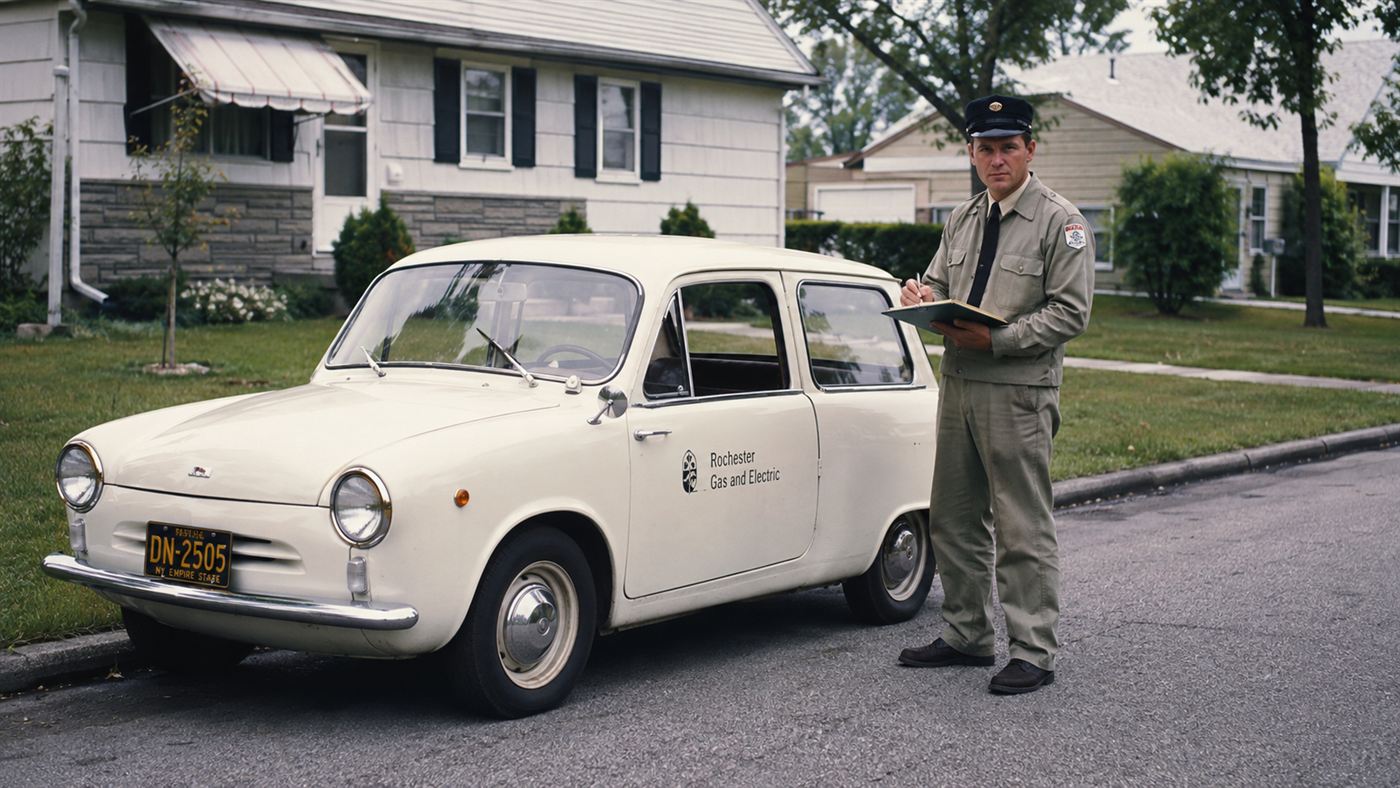 A 1960s utility worker beside a small electric company car like the Henney Kilowatt